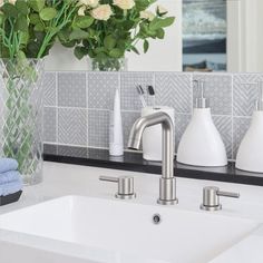 a bathroom sink with soap dispensers and flowers in a vase on the counter