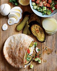 an assortment of food is displayed on a cutting board, including vegetables and pita bread