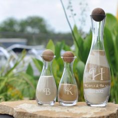 three glass bottles with sand in them sitting on a stone slab next to some plants