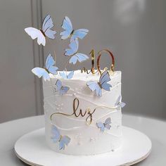 a white cake with blue butterflies and the number one on top is decorated with gold lettering