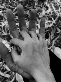 two hands reaching up towards each other in front of some grass and dirt, with one hand holding the other