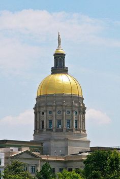 a golden dome on top of a building with trees in the foreground and blue sky behind it