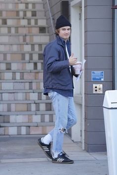 a young man is walking down the sidewalk while holding his coffee and wearing a beanie