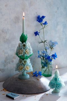 two candles are sitting on a table next to some blue and white flowers in vases