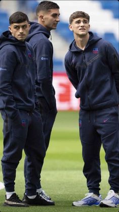 three men standing on a soccer field with one wearing a hoodie and the other in sweatpants