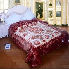 a bed with a red bedspread and white pillows in a room that has paintings on the walls