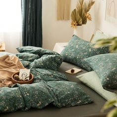 an unmade bed with green and white comforter on it, next to potted plants