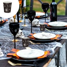 a table set for halloween with black and white plates, silverware and candlesticks