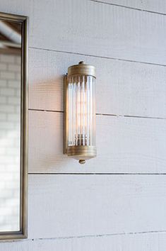 a wall mounted light on the side of a white building with a mirror above it