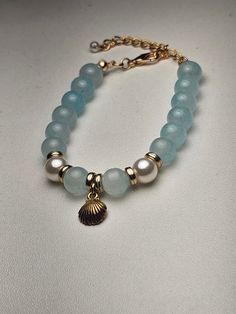 Dive into coastal elegance with our "Ocean Breeze Bracelet." This stunning piece features light blue beads intertwined with delicate gold accents, perfectly complemented by lustrous pearls that evoke the serenity of the sea. The centerpiece is a beautiful shell pendant, adding a touch of beachy charm to the design. Whether you're dressing up for a special occasion or adding a touch of oceanic beauty to your everyday look, this bracelet is sure to make a statement. Handcrafted with care, it's a perfect gift for someone special or a lovely treat for yourself. - Materials : Light blue beads, gold accents, pearls, shell pendant - Length : 6 inches Embrace the essence of the sea with this elegant bracelet that effortlessly captures the beauty of the ocean. Elegant Gold Pearl Bracelet For Summer, Gold Bracelet With Pearl Charm For Beach, Summer Gold Beaded Pearl Bracelet, Gold Pearl Charm Bracelet For Beach, Gold Pearl Bracelet With Pearl Charm For Beach, Elegant Beaded Pearl Bracelet For Summer, Elegant Light Blue Jewelry With 8mm Beads, Elegant Light Blue Summer Jewelry, Beach Jewelry With 8mm Blue Beads