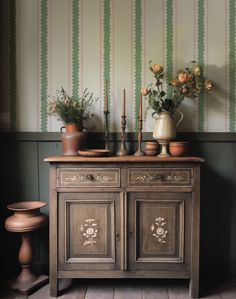 an old dresser with vases and flowers on it in front of a striped wall