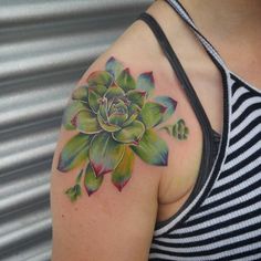 a woman's shoulder with a flower tattoo on her left arm, and green leaves around it