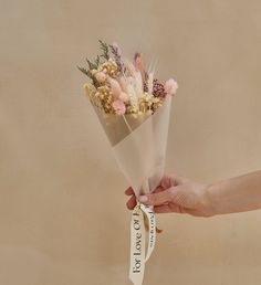 a hand holding a bouquet of flowers with a ribbon around it that says i love you