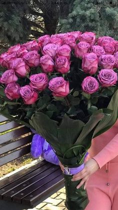 a woman sitting on a bench holding a large bouquet of pink roses