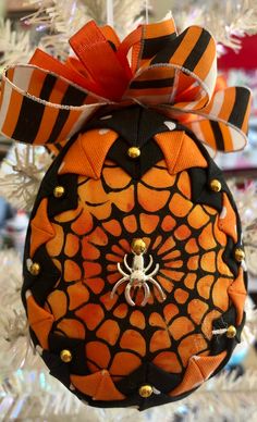 an ornament hanging from a christmas tree decorated with orange and black spider webs