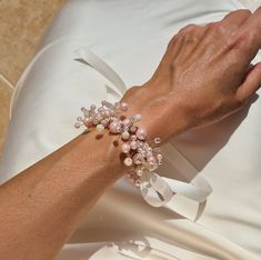 a woman's arm wearing a white bracelet with pearls and bows on it,