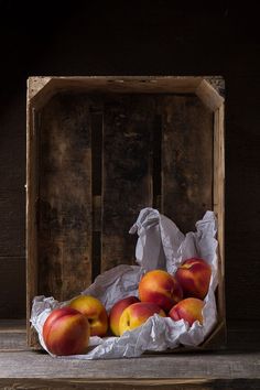 a wooden box filled with ripe peaches on top of a wood table next to a white paper bag