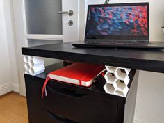 an open laptop computer sitting on top of a black desk next to a red book