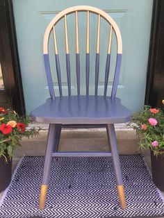 a blue wooden chair sitting in front of a door with flowers on the doorstep mat