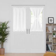 two white curtains hanging on the side of a door with bookshelves and potted plants