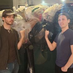 two men standing next to each other in front of bags of garbage and trash cans