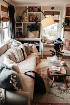 a living room filled with lots of furniture and pillows on top of a rug next to a window