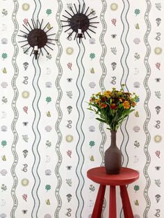 a vase with flowers on a small table in front of a wallpapered background