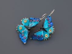 Handmade blue butterfly earrings featuring dichroic glass. Unique and lightweight, these drop earrings are crafted with care Crafted by skilled artisans, these unique earrings showcase the delicate beauty of butterflies. The iridescent blue dichroic glass wings shimmer in the light, capturing the essence of a fluttering butterfly. Lightweight and comfortable, they dangle gracefully, adding a touch of nature-inspired elegance to any outfit. Whether you're attending a garden party or simply want t Blue Butterfly Jewelry With Butterfly Print, Blue Butterfly Print Jewelry As A Gift, Blue Butterfly Print Jewelry For Gifts, Blue Jewelry With Butterfly Print For Gift, Blue Butterfly Charm Dangle Earrings, Handmade Blue Butterfly Earrings, Blue Butterfly Charm Earrings For Gift, Blue Dangle Earrings With Butterfly Charm, Blue Butterfly Earrings For Gift