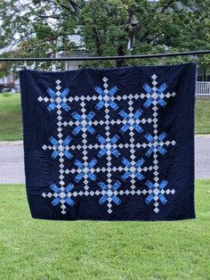 a blue and white quilt hanging from a clothes line in the grass near a tree