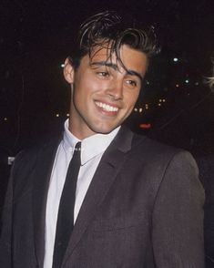 a young man in a suit and tie smiling at the camera with his hand on his hip