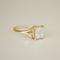 a yellow gold ring with an emerald cut diamond in the center, sitting on a white surface