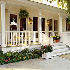 a white house with flowers and potted plants on the front porch