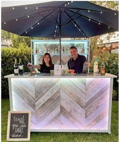 a man and woman standing behind a bar with an umbrella over it that has lights on