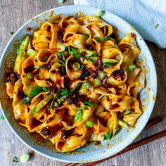 a bowl filled with pasta and vegetables on top of a wooden table next to chopsticks