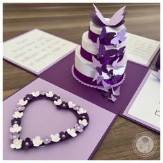 a purple and white wedding cake on top of a table next to some greeting cards