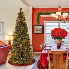 a decorated christmas tree in the corner of a dining room with red walls and chairs