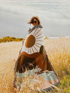 a woman is sitting in the grass wearing a blanket