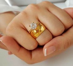 a woman's hand holding a gold ring with a diamond on it and a white shirt in the background