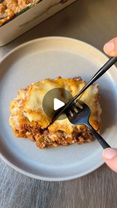 a person is holding a fork and eating lasagna casserole on a plate