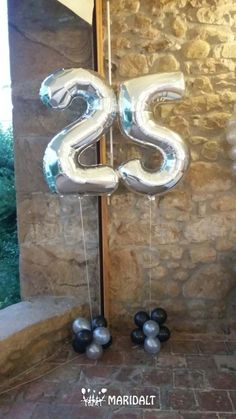 the number twenty five balloons are hanging in front of a stone wall