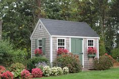 a garden shed with flowers around the windows and shutters on the door is shown