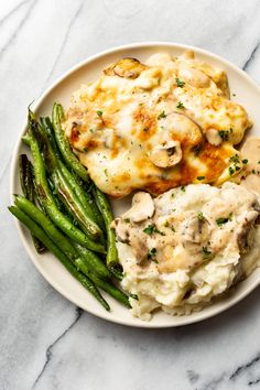 a white plate topped with chicken, mashed potatoes and asparagus next to green beans