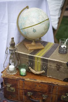 an old suitcase with a globe on top and other items sitting on it, along with some candles