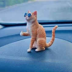 an orange and white cat sitting on the dashboard of a car with sunglasses in it's eyes