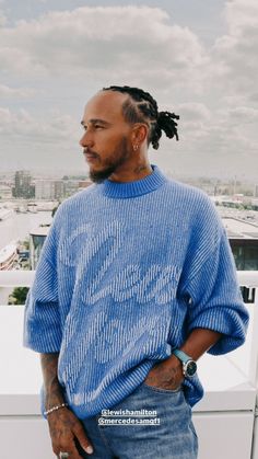 a man with dreadlocks standing on top of a building wearing a blue sweater