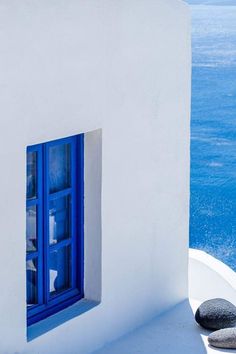 a blue window on the side of a white building with water and sky in the background