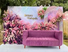 a purple couch sitting in front of a floral backdrop with pink flowers and greenery