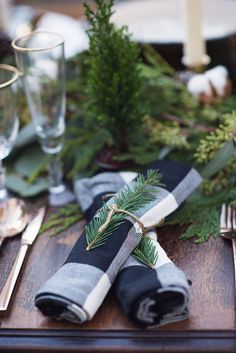 a place setting with napkins, silverware and evergreen leaves on the table cloth