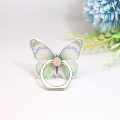 a butterfly shaped ring sitting on top of a white table next to blue and green flowers