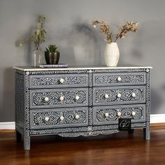 an ornate black and white chest of drawers with flowers in vases on the top